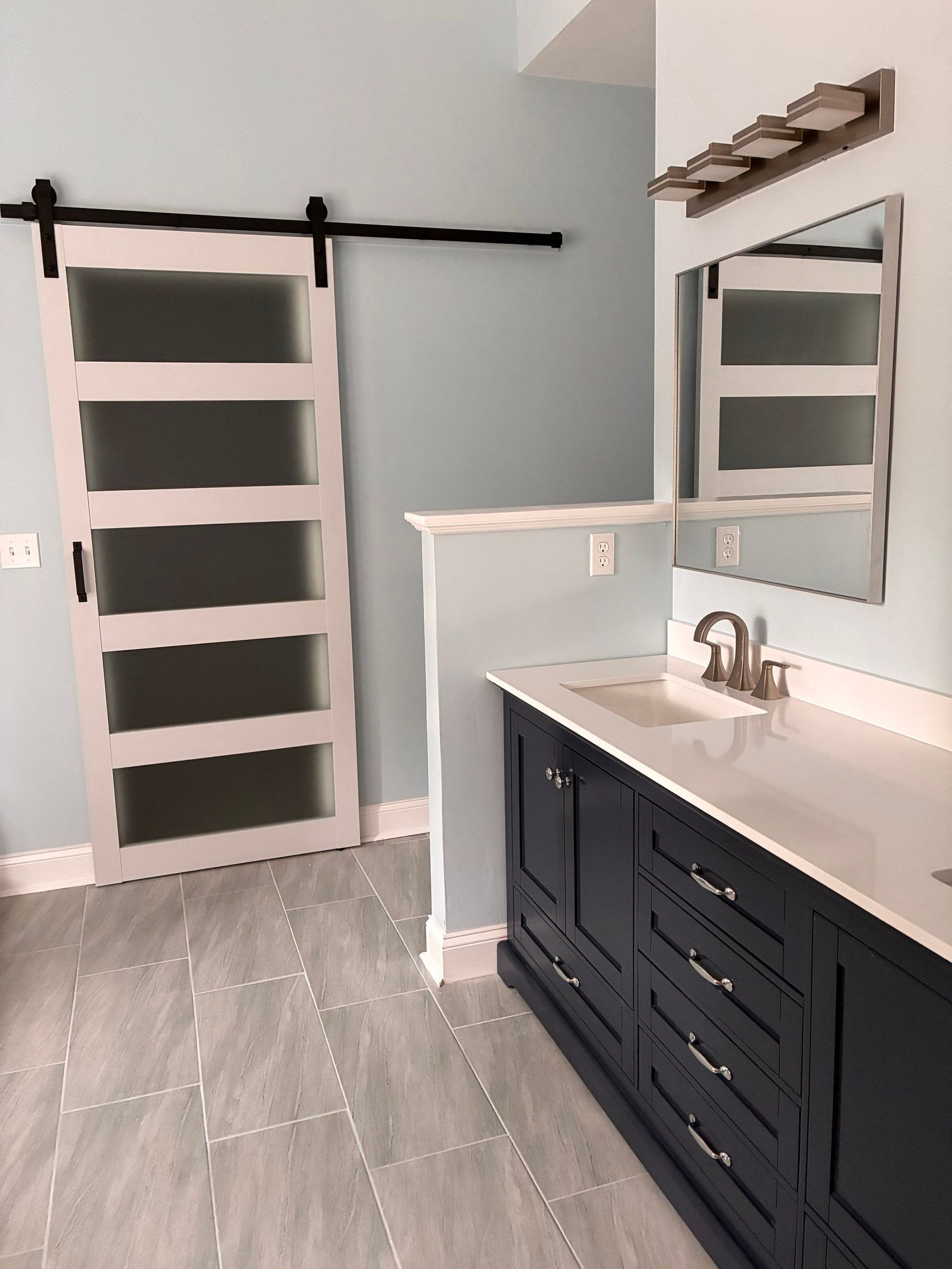 Bathroom with navy vanity, white countertop, light blue walls, frosted glass door.
