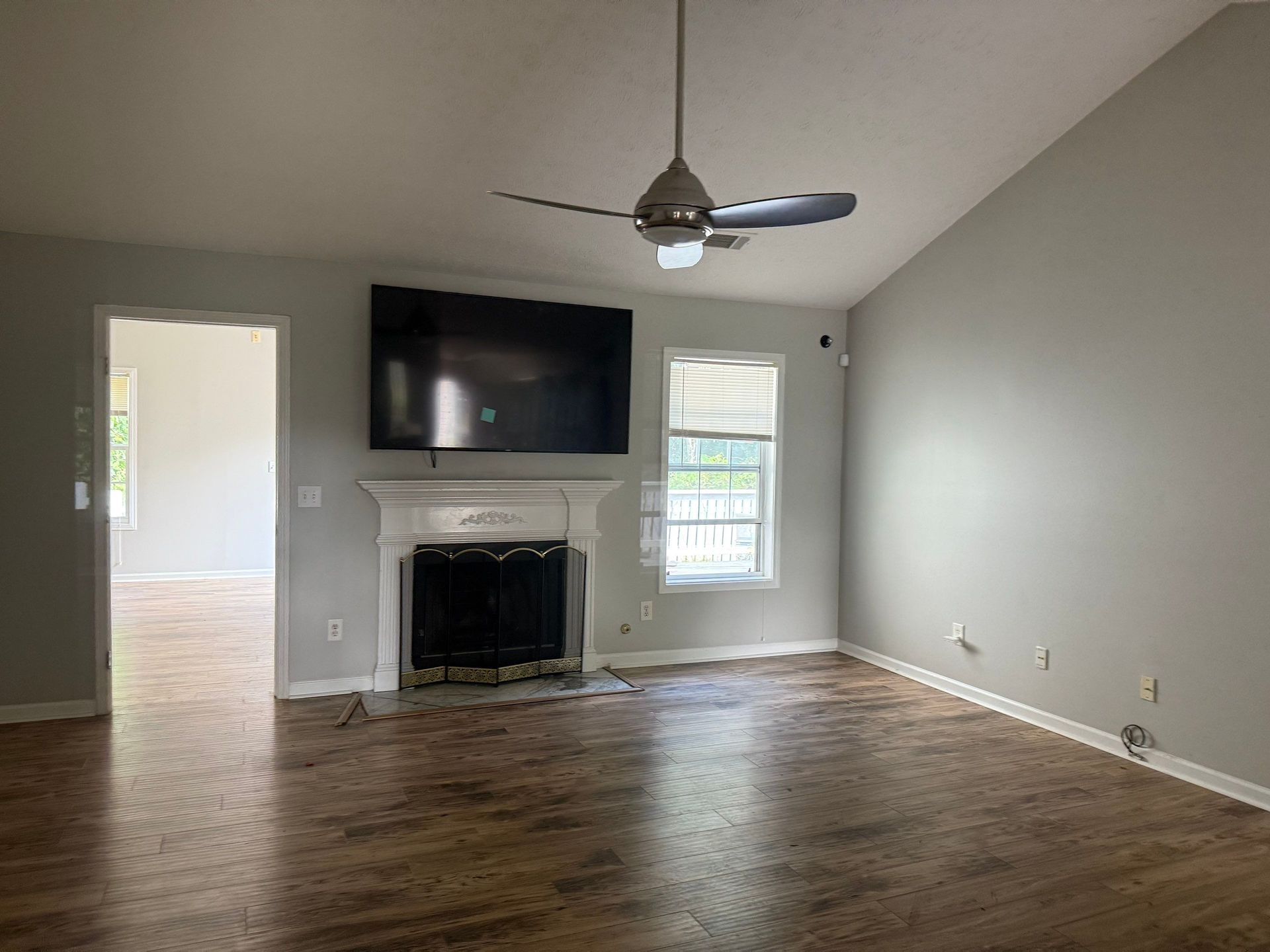 Living room with TV above fireplace, window, and hardwood floors. Gray walls.