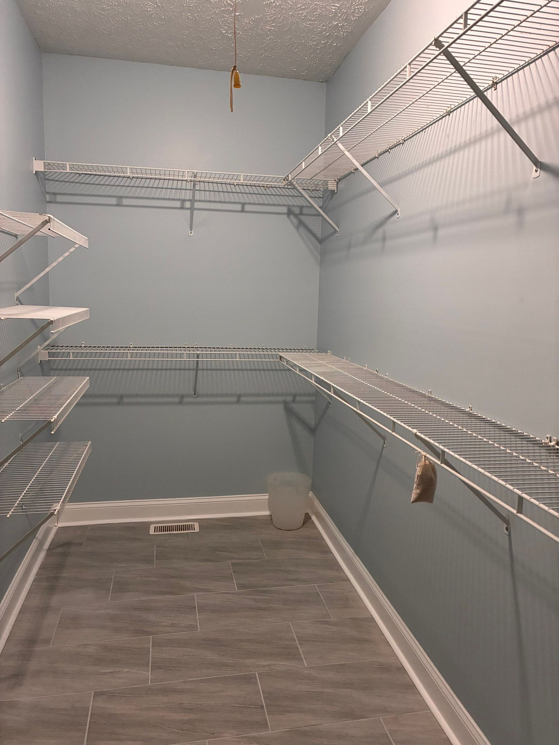 Empty walk-in closet with blue walls, wire shelving, and gray tile floor.