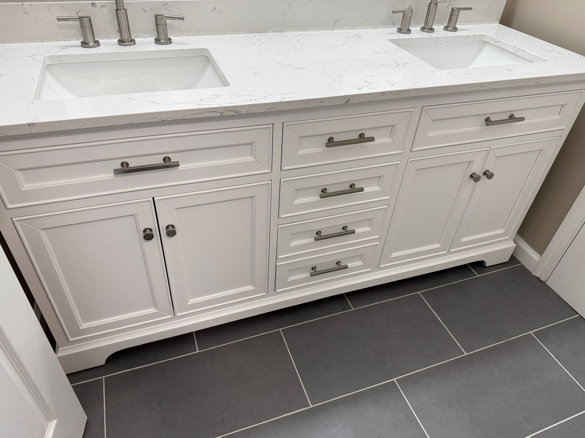 White double sink vanity with brushed nickel hardware, set against gray tile floor.