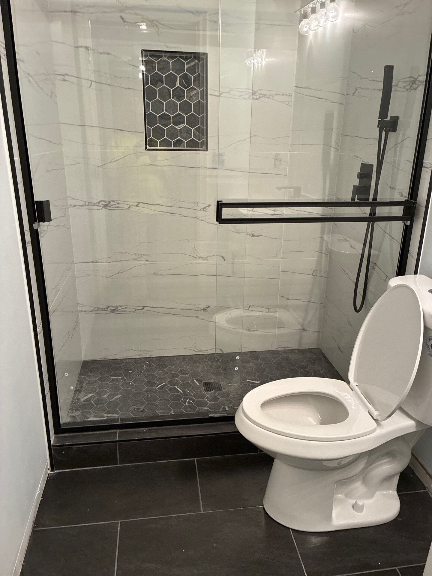Bathroom with glass shower, toilet, and dark tile floor.