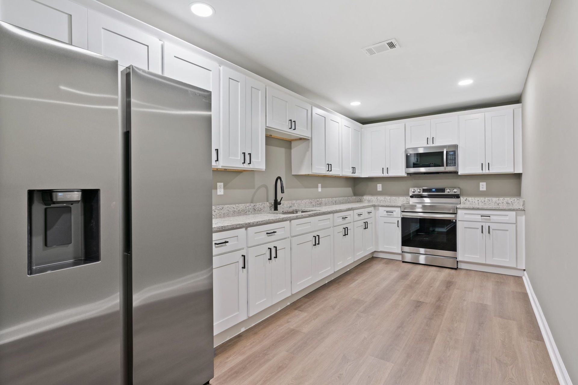 White kitchen with stainless steel appliances, white cabinets, and light wood flooring.