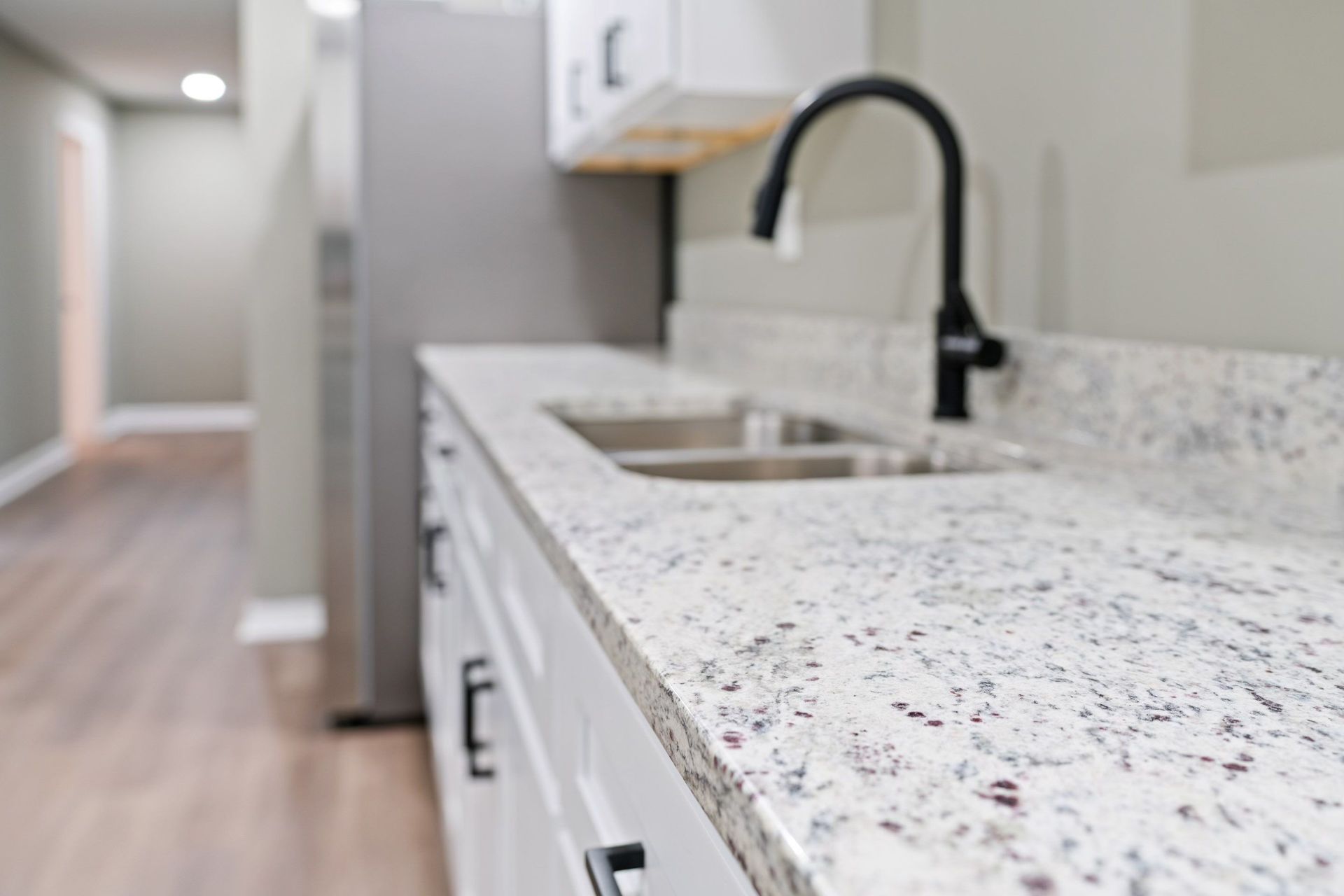 White granite countertop with black faucet and cabinets in a kitchen.