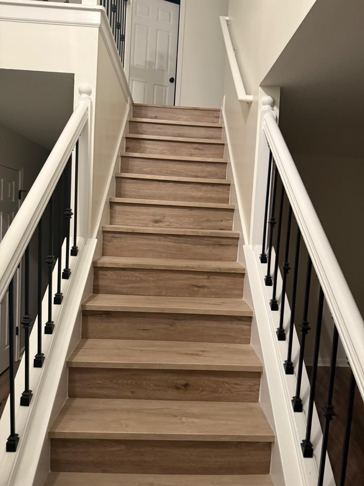 Wooden staircase with white railings and black wrought iron spindles.
