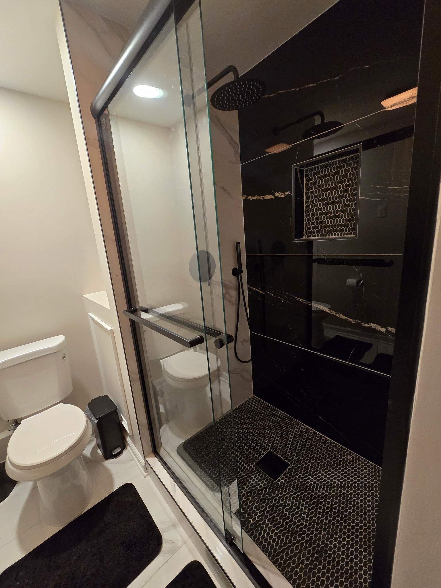 Modern bathroom with black tile shower, glass door, and white toilet.