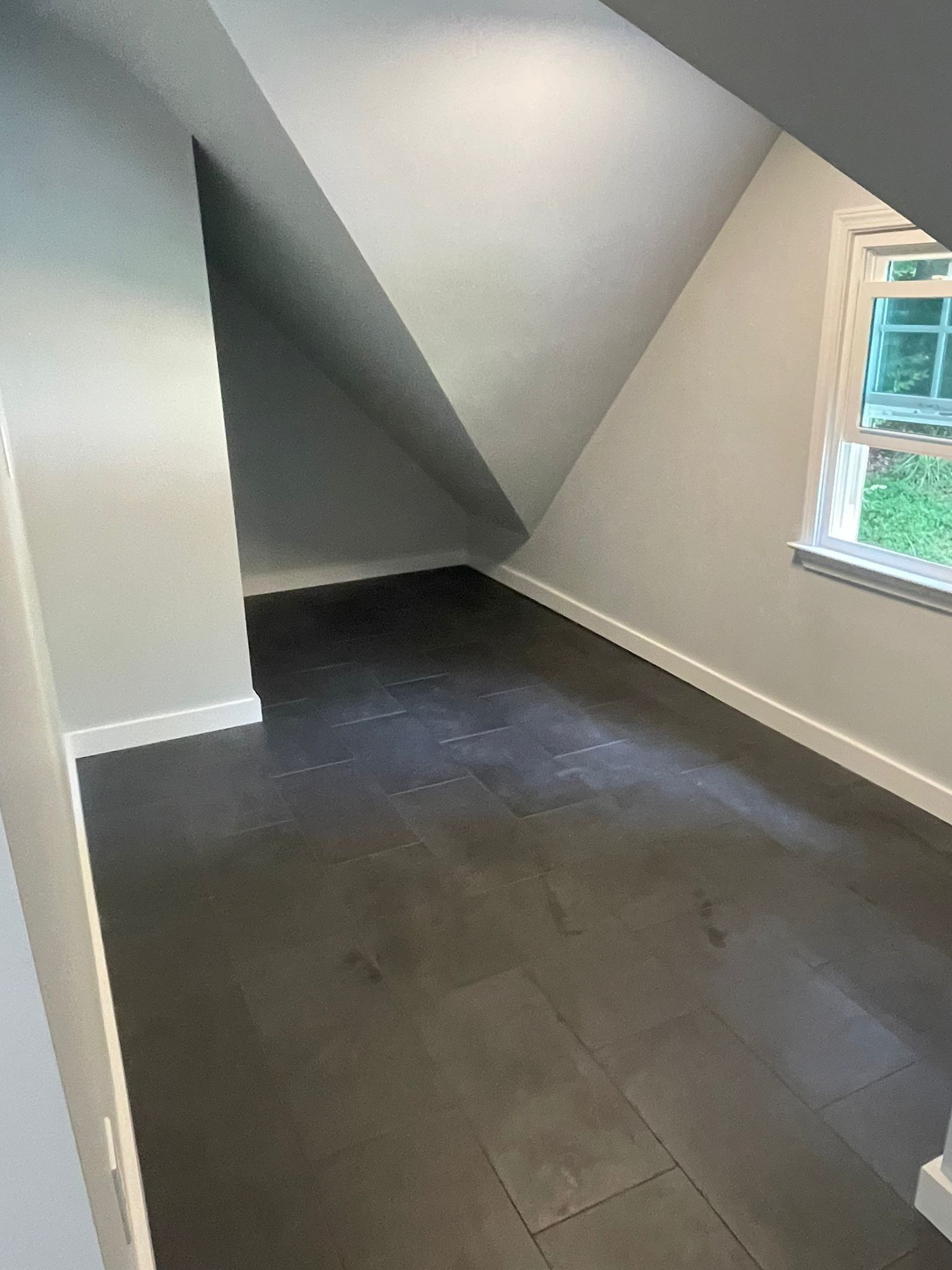 Empty attic room with dark wood floor, sloped ceilings, and small window.