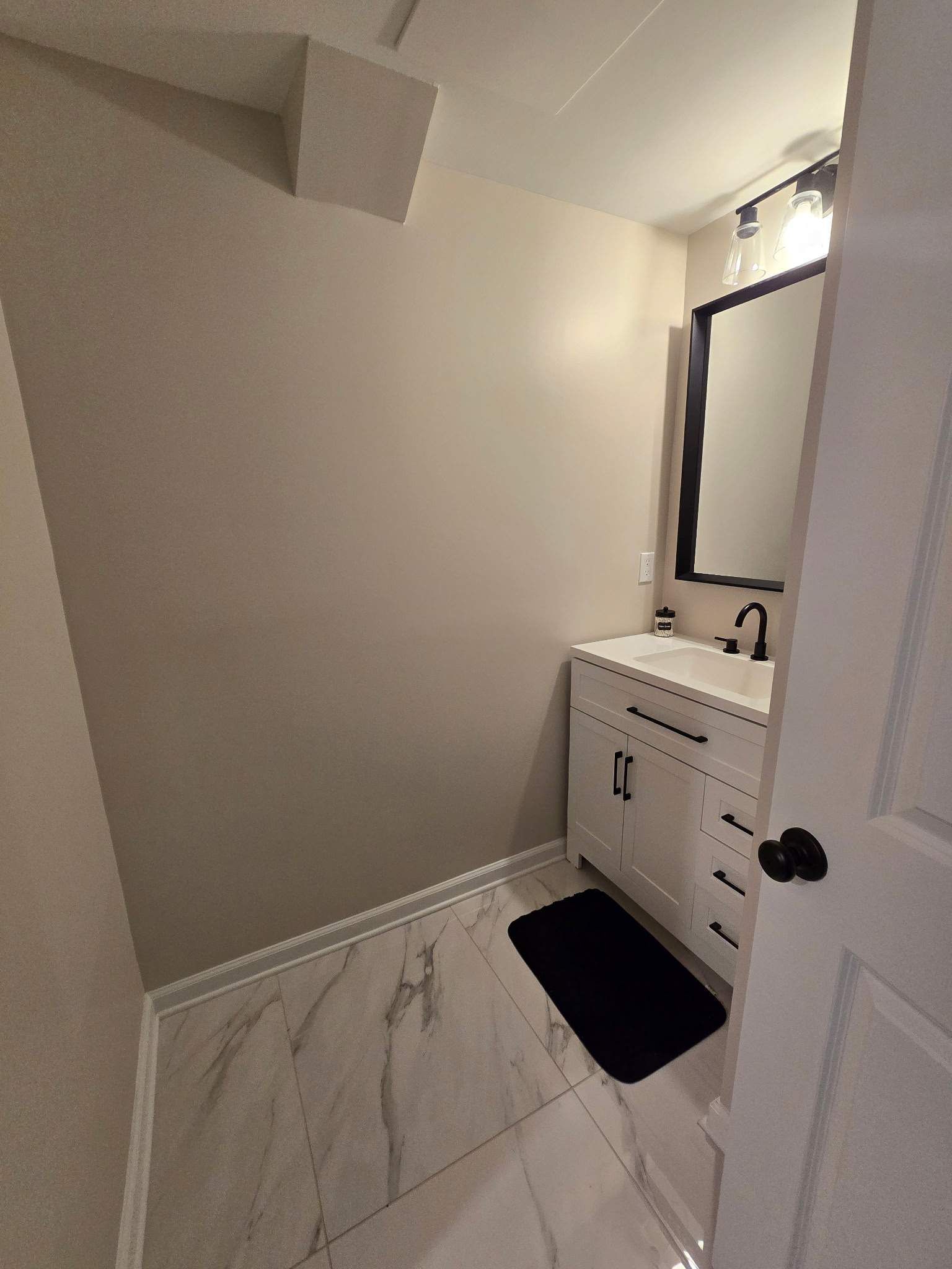 Small bathroom with white vanity, black faucet, and marble-like tile.