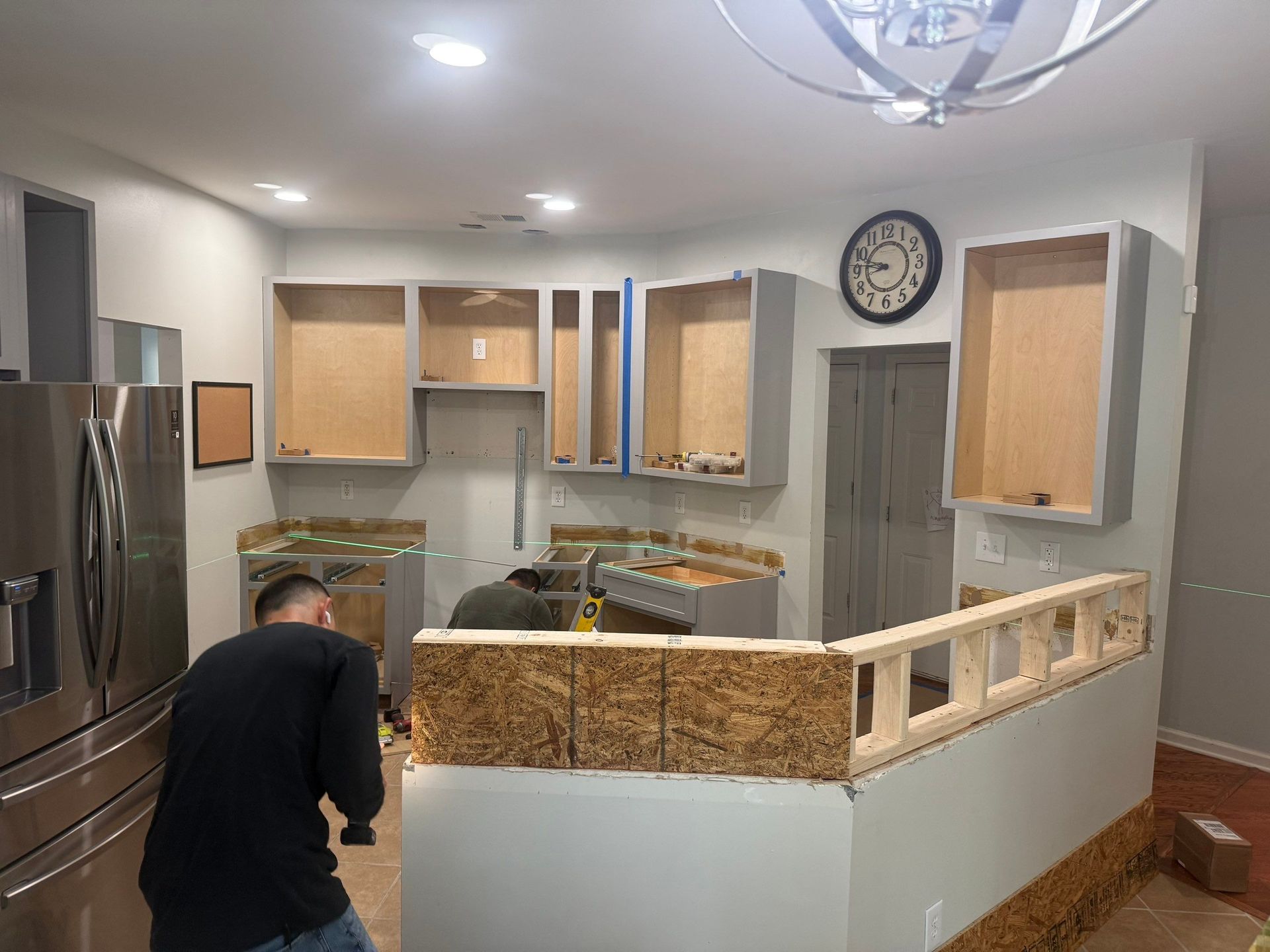 Kitchen under renovation, cabinets hung, island construction. Two workers in action.
