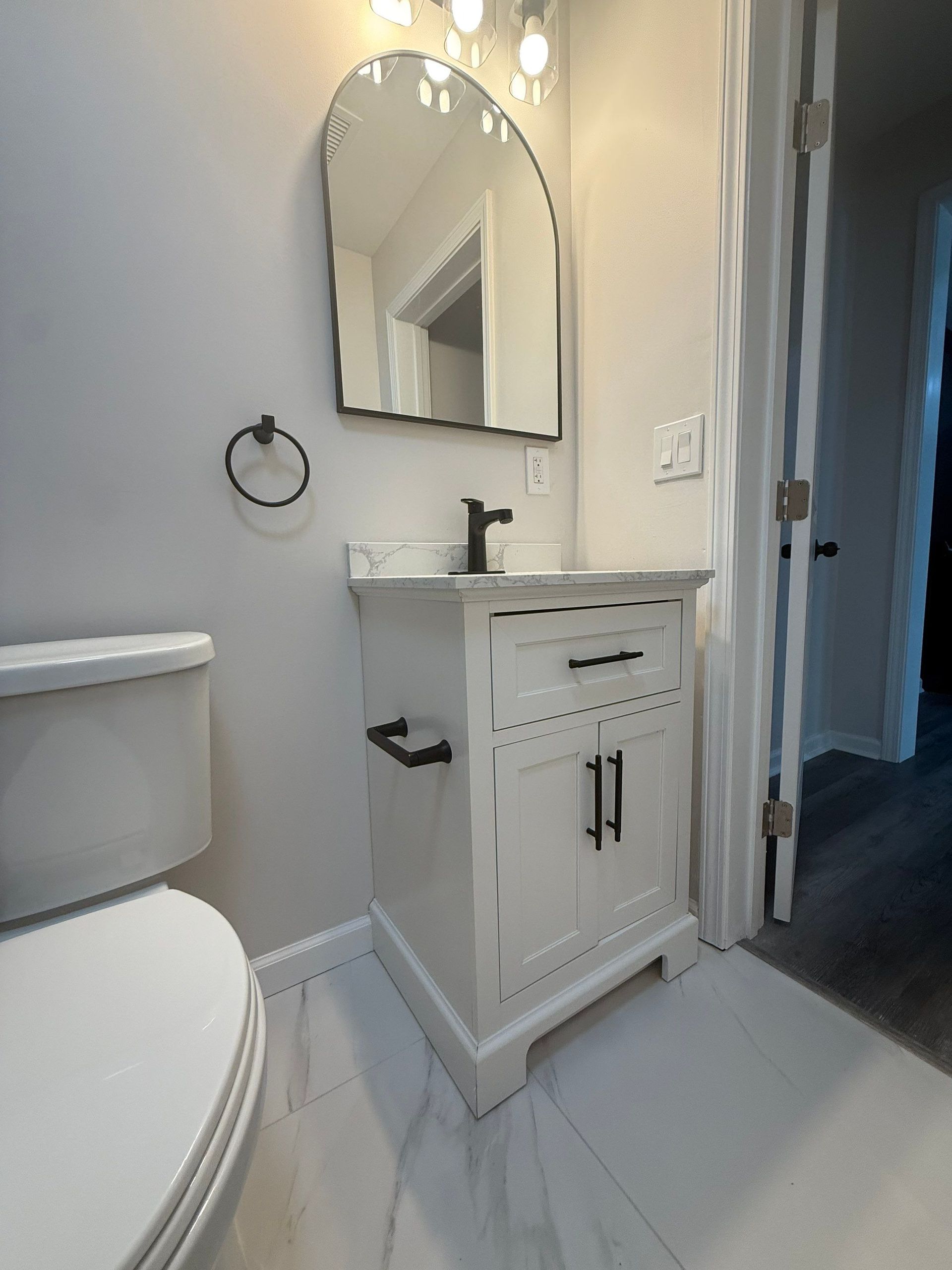 Small white bathroom with vanity, toilet, and arched mirror.