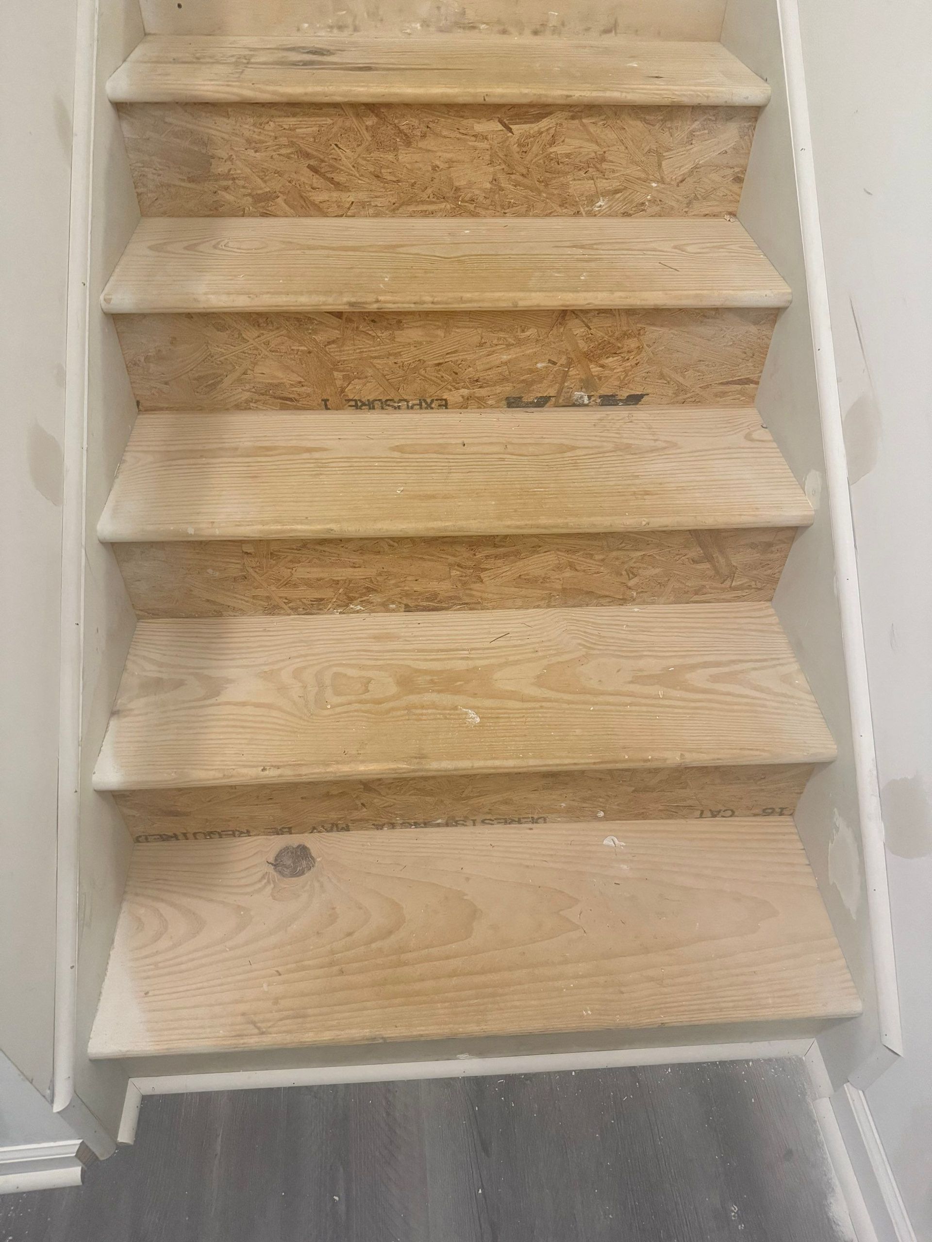 Staircase with light wooden steps, white trim, and a wall on the right side.