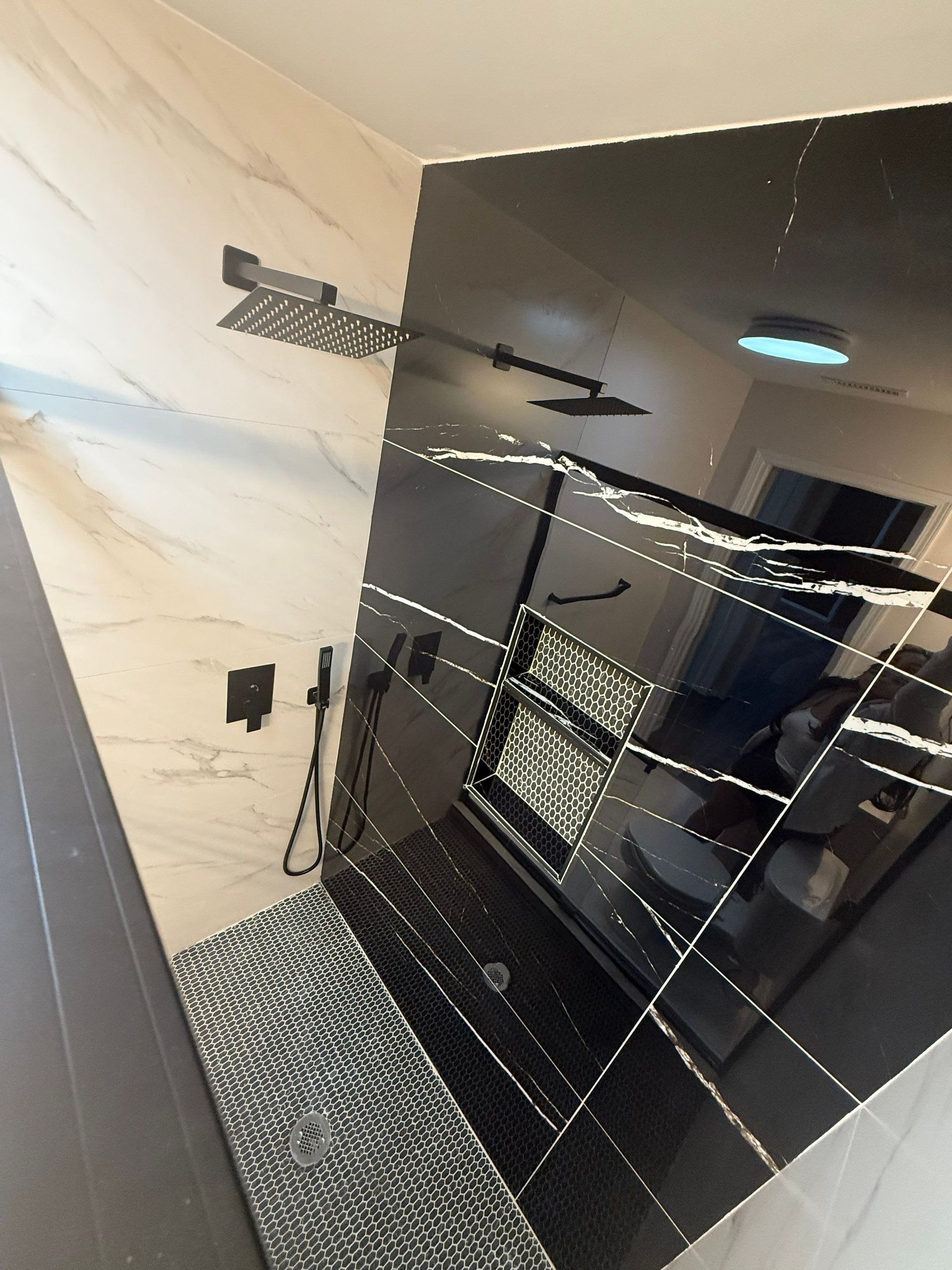 Modern bathroom with black and white tile shower, featuring multiple showerheads.