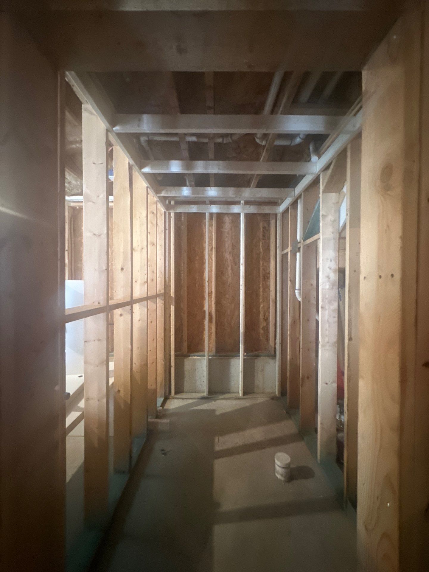 Interior view of a framed hallway under construction, with wood studs and concrete flooring.