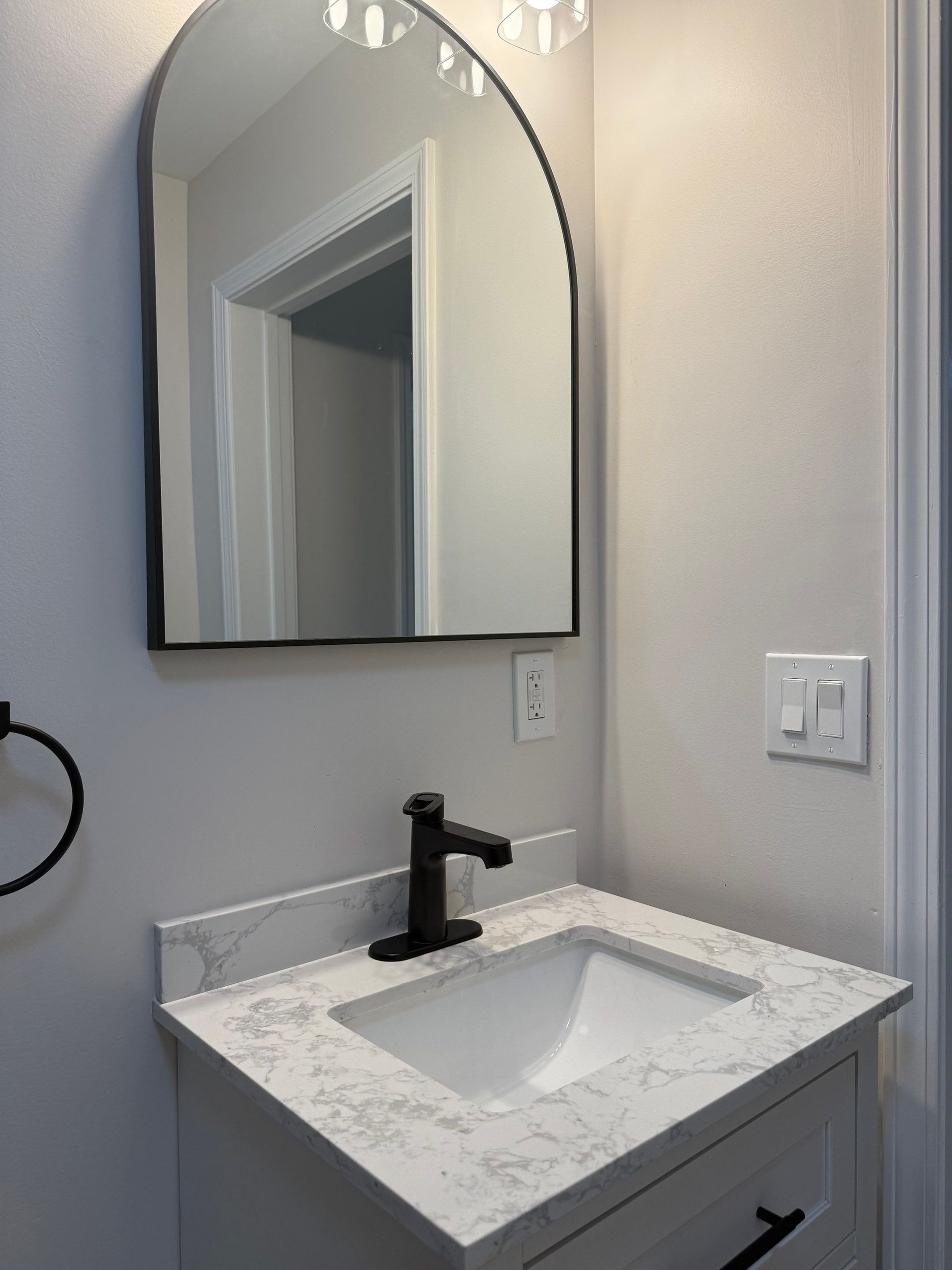 Small bathroom with white vanity, quartz countertop, black faucet, and arched mirror.