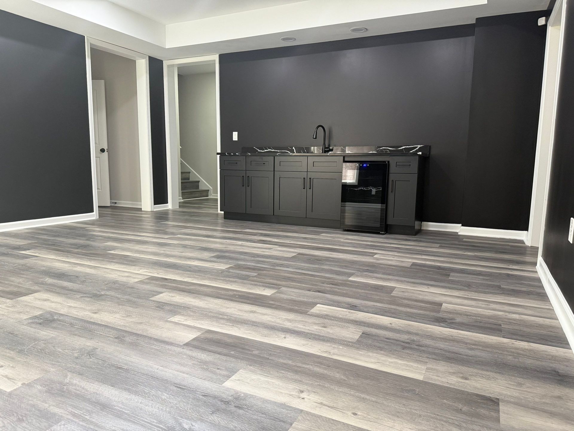 Gray wood-look flooring in a mostly empty room with a dark gray bar and a staircase.