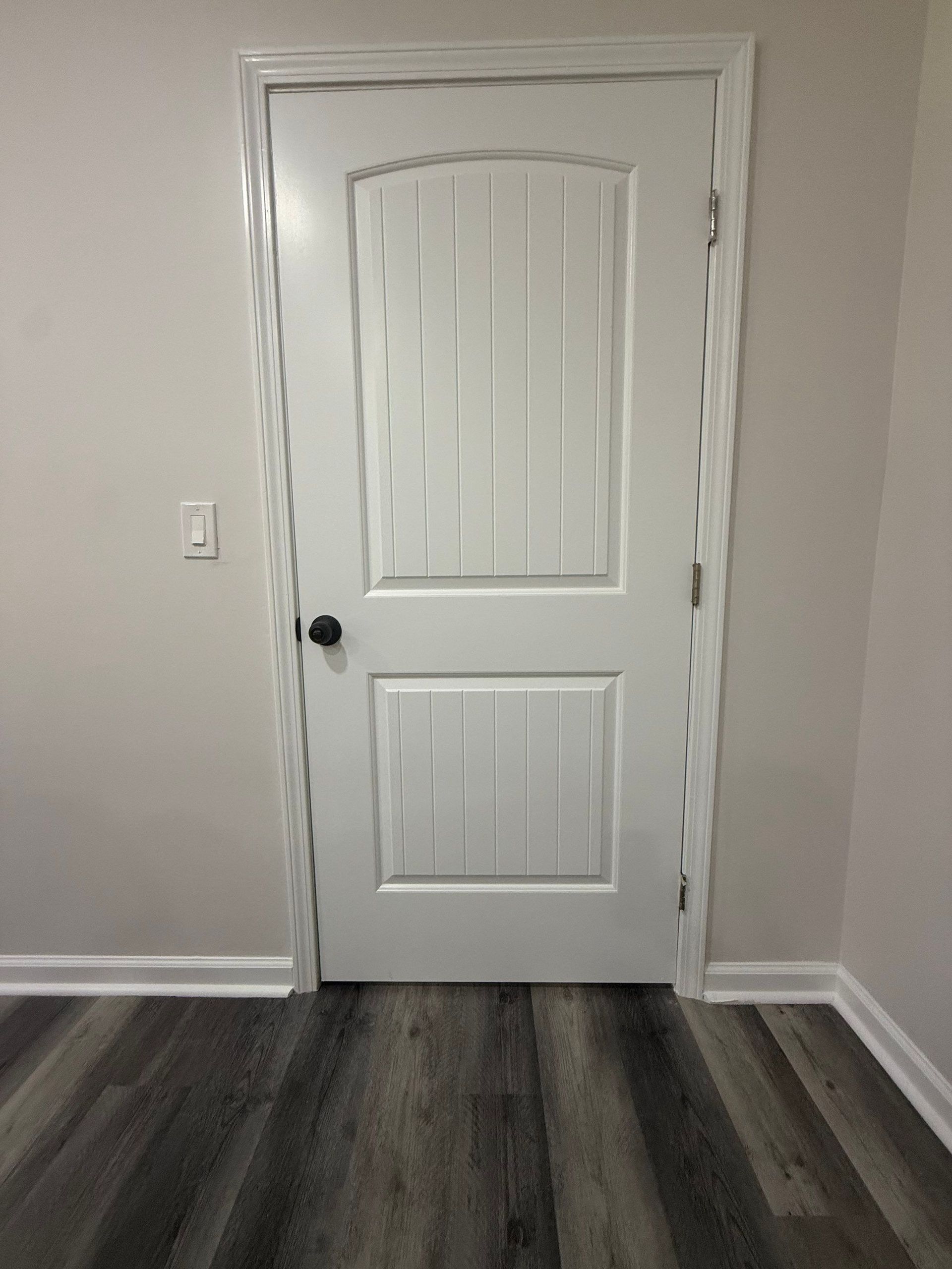 White interior door with black doorknob, light switch, and gray and white flooring.