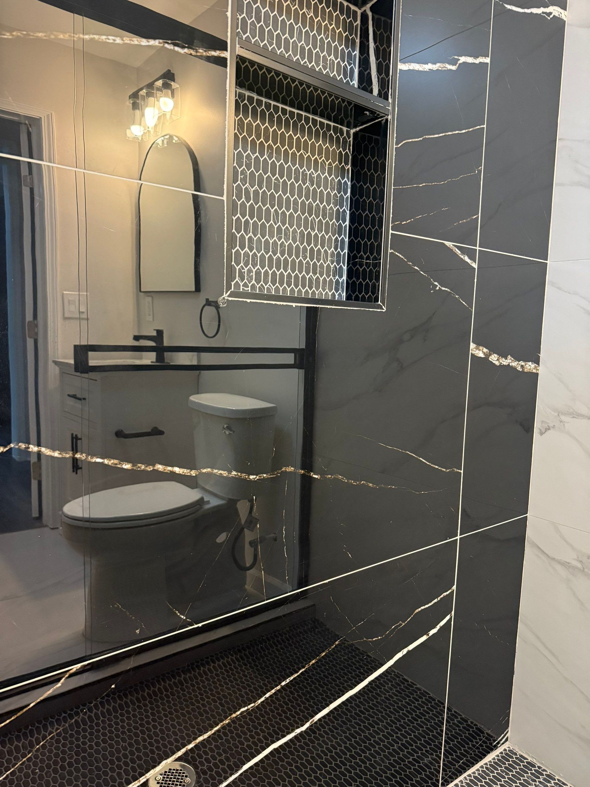 Modern black and white bathroom with marble tiles, black fixtures, and a white toilet.