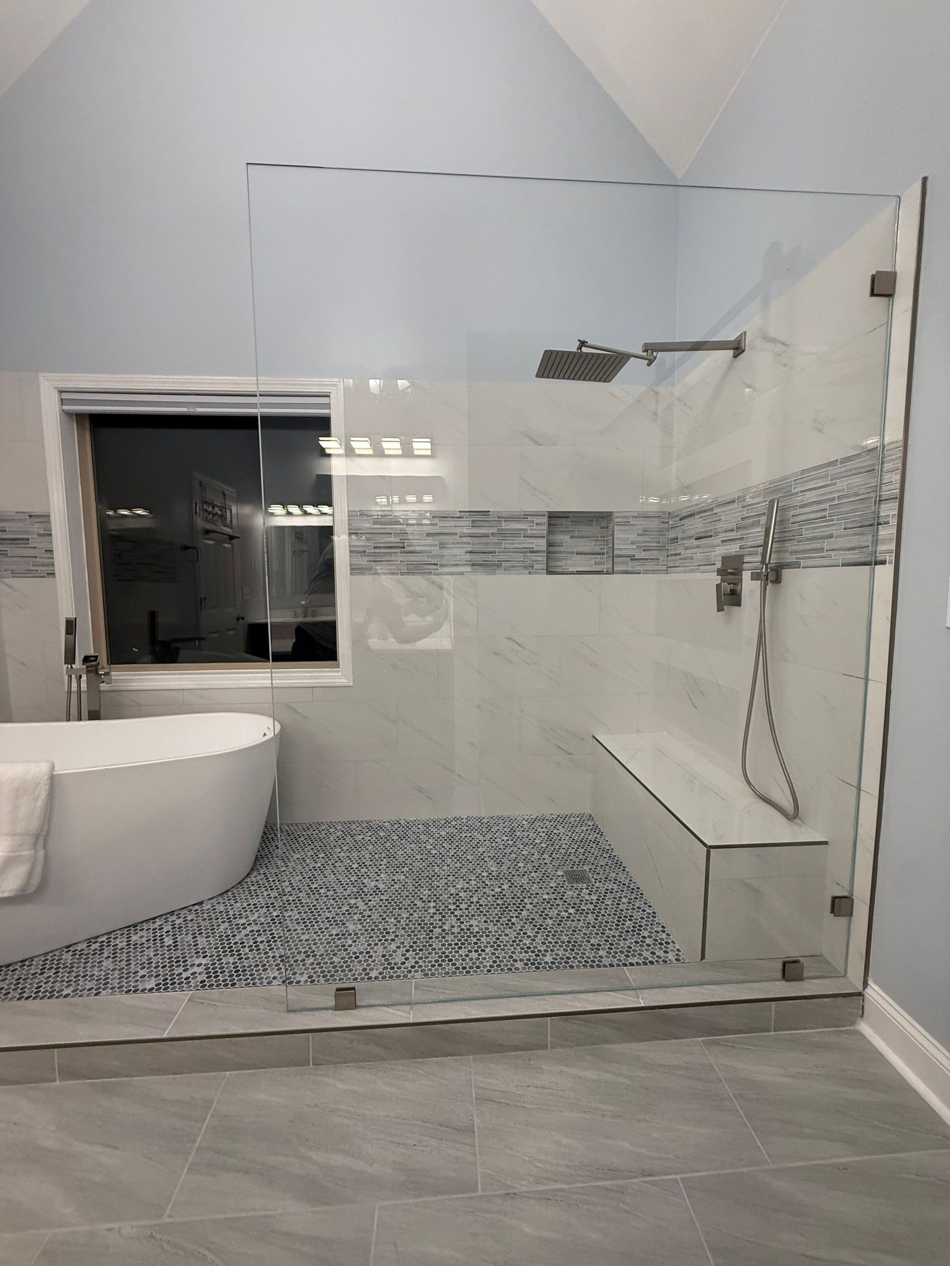 Spacious bathroom with glass shower, soaking tub. Blue, white tile, mosaic floor.