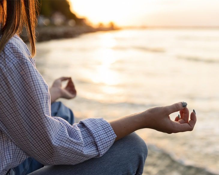 A woman is sitting in a lotus position on the beach.