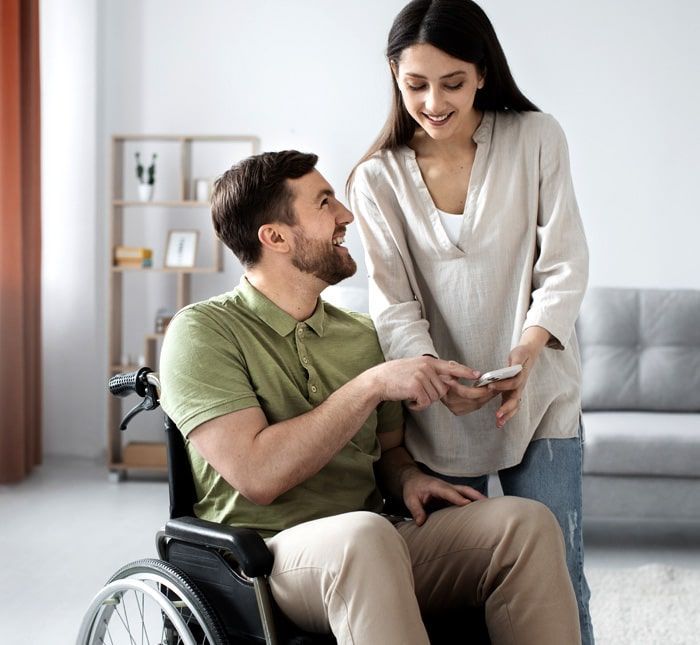 A woman is standing next to a man in a wheelchair.