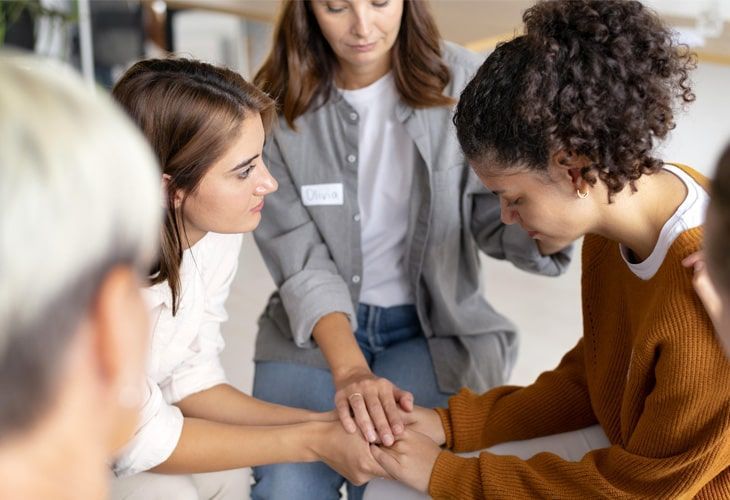 A group of people are sitting around a table putting their hands together.