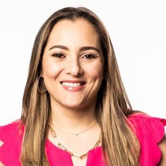 A woman in a pink shirt and necklace is smiling for the camera.