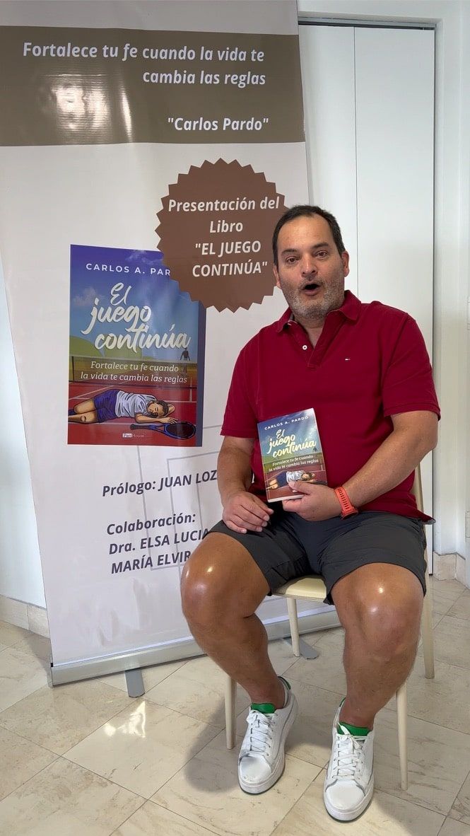 A man in a red shirt is sitting in a chair holding a book.