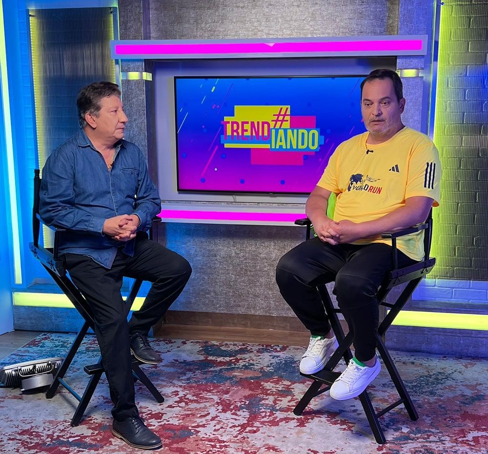 Two men are sitting in front of a tv screen that says trend lando