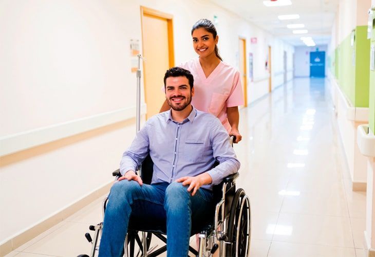 A smiling man in a wheelchair carried by a nurse