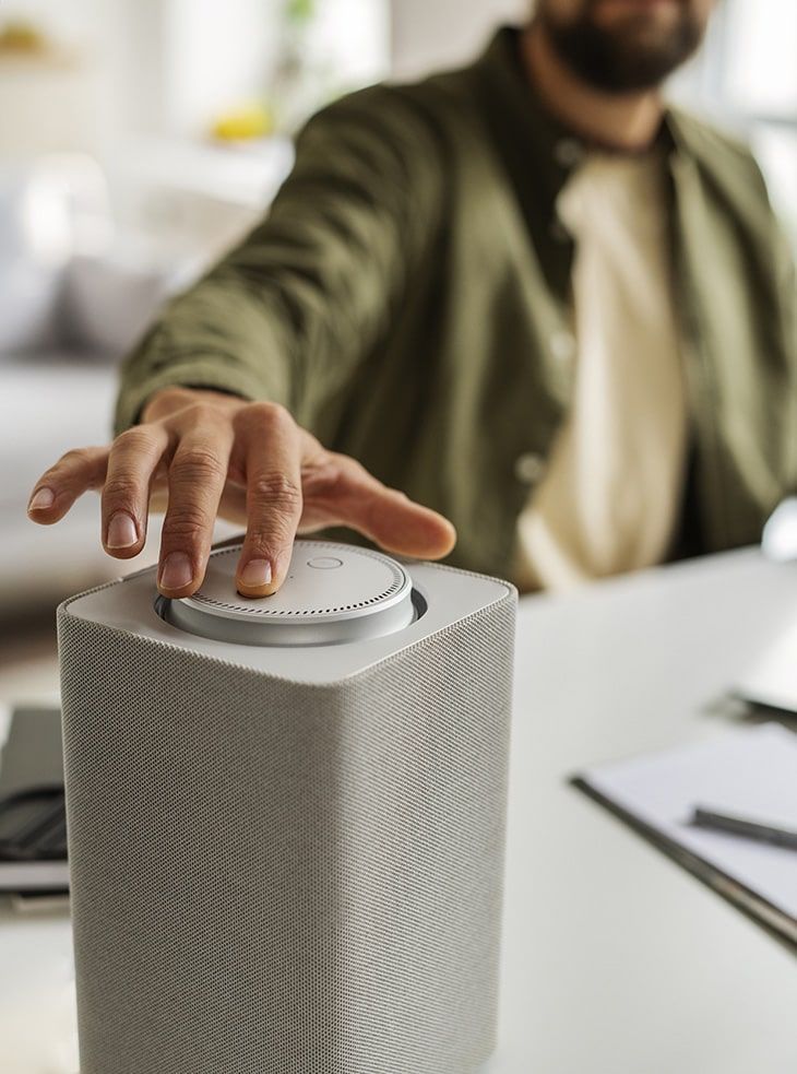 A man is sitting at a desk using a smart speaker.