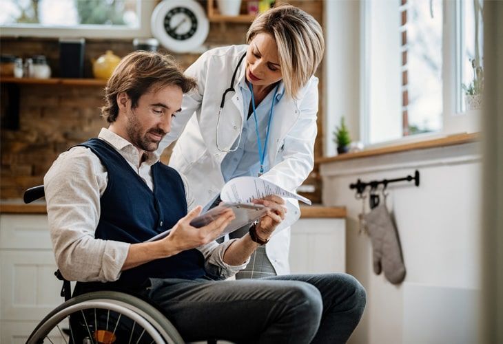 A doctor is talking to a man in a wheelchair who is looking at a tablet.