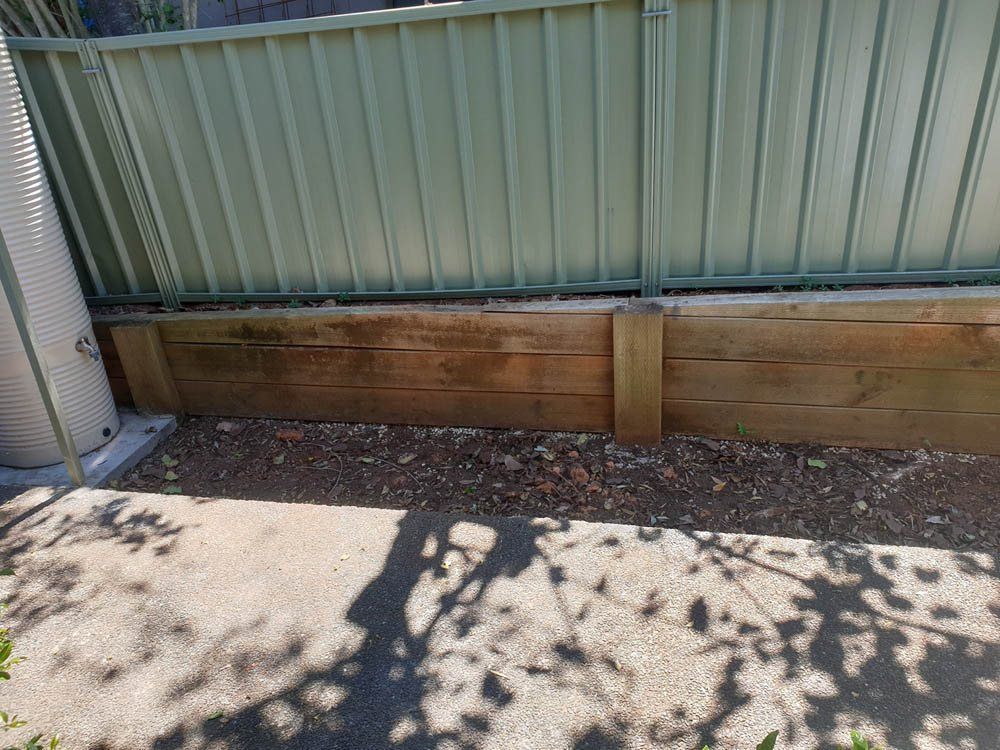 A Wooden Fence is Sitting Next to a Metal Fence — Greener Gardens Gardening Service In Thrumster, NSW