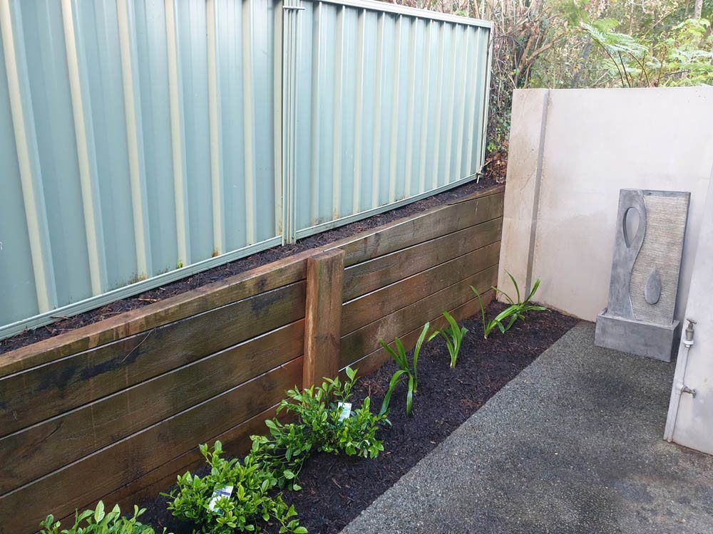 A Wooden Fence Surrounds a Garden With Plants and a Fountain — Greener Gardens Gardening Service In Thrumster, NSW