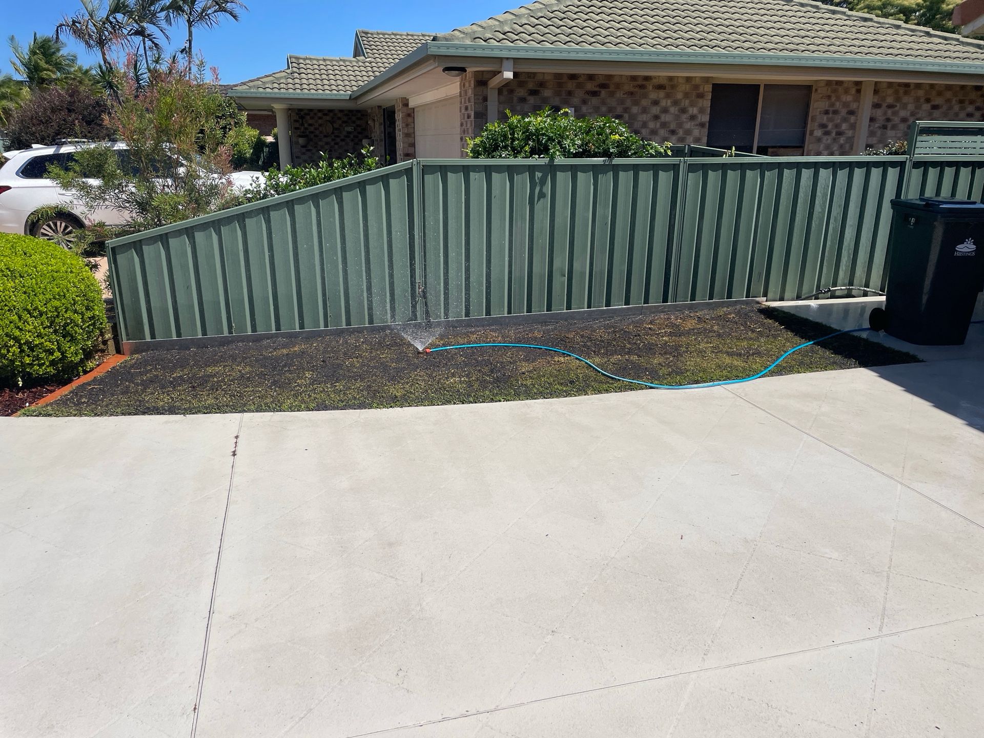 A green fence surrounds a driveway in front of a house. — Greener Gardens Gardening Service In Thrumster, NSW