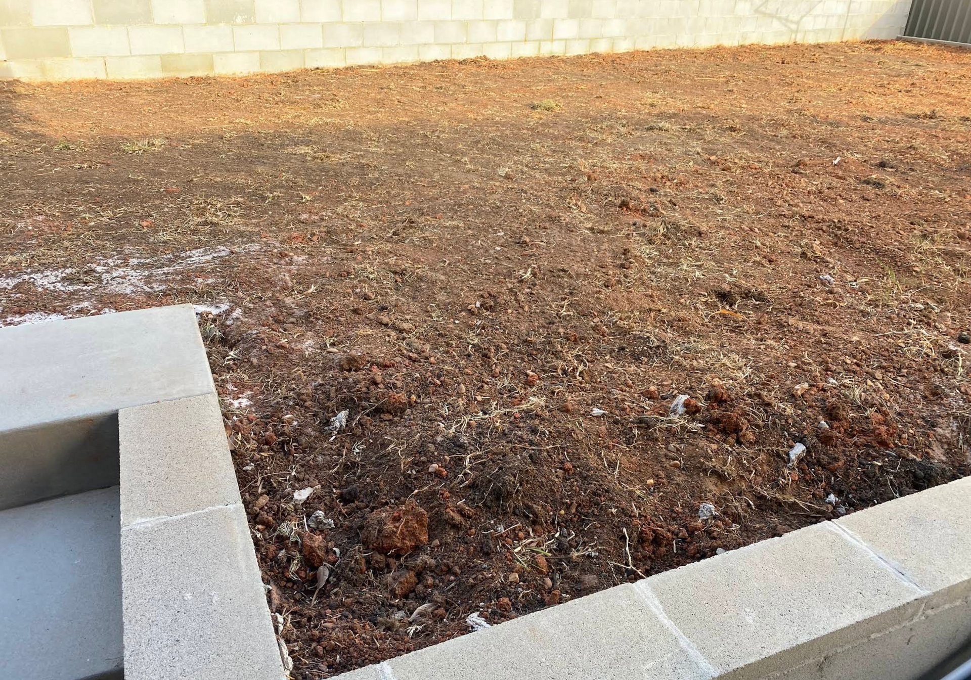 A brick wall surrounds a pile of dirt in a yard — Greener Gardens Gardening Service In Thrumster, NSW