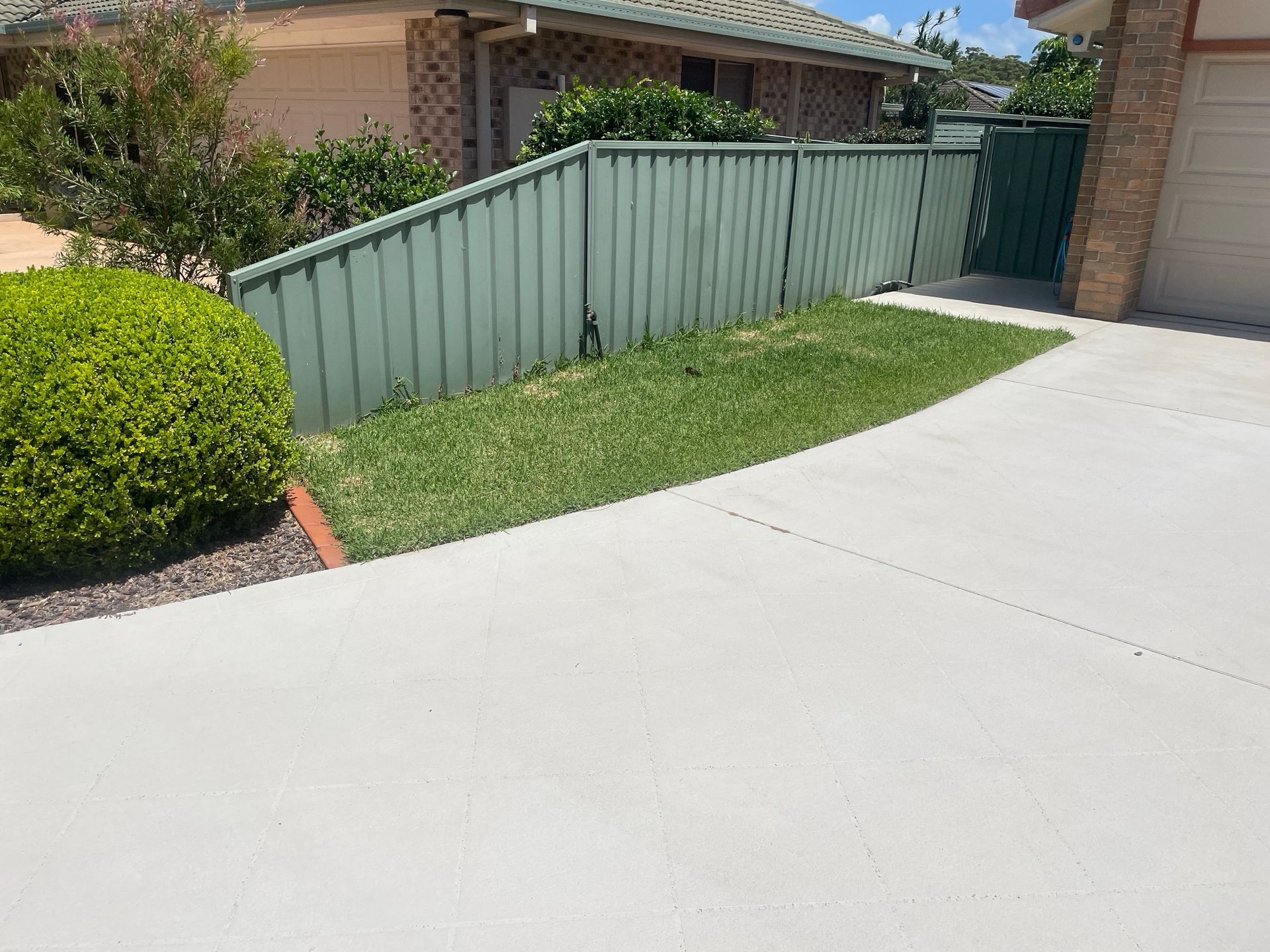 A green fence surrounds a lush green lawn in front of a house. — Greener Gardens Gardening Service In Thrumster, NSW