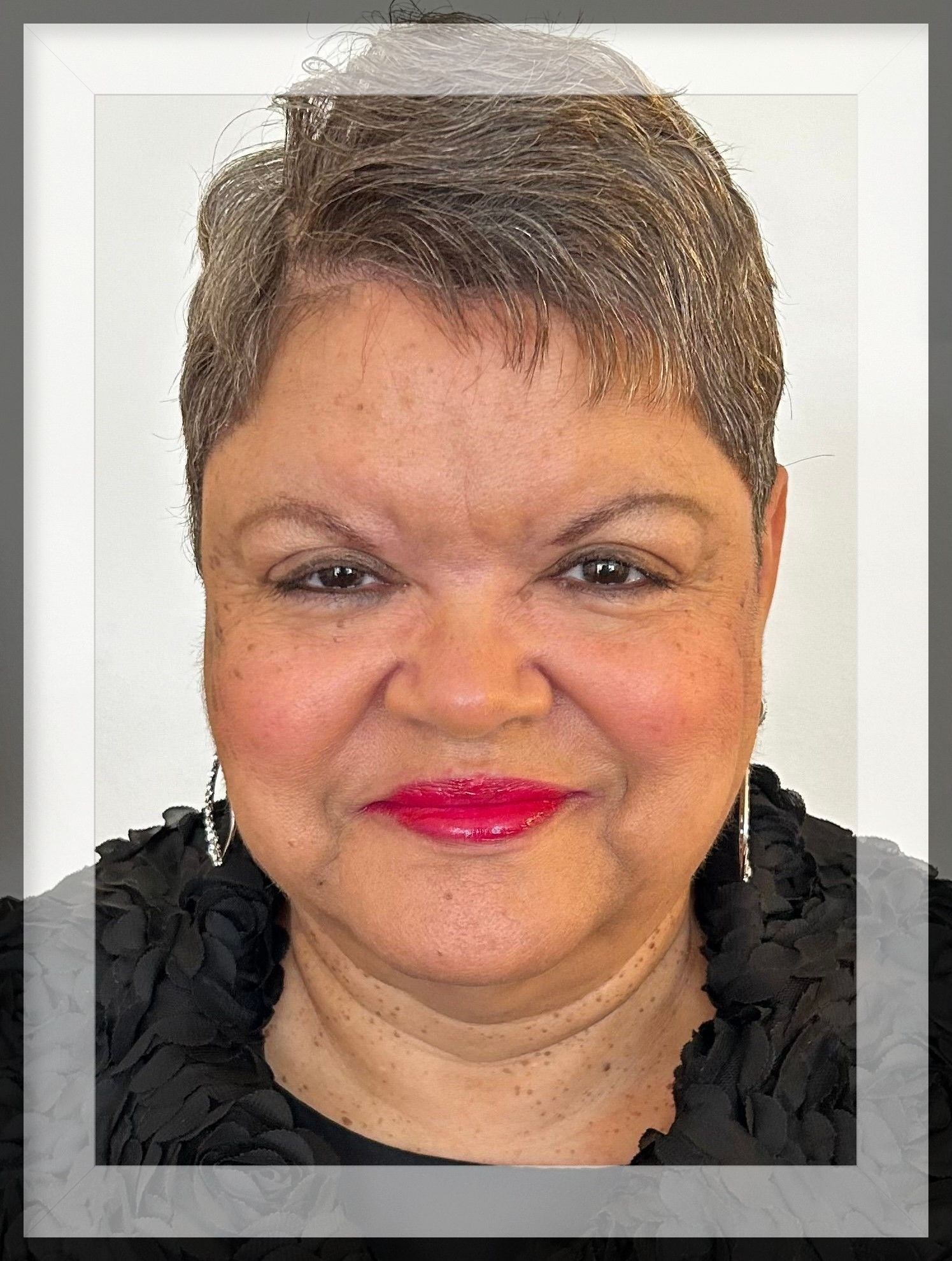 Smiling Black woman with short gray hair, red lipstick, black jacket, and dangling earrings.