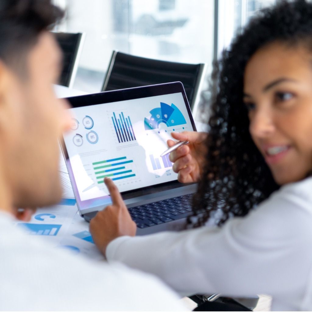Woman points at laptop screen displaying charts, collaborating with a man in an office.