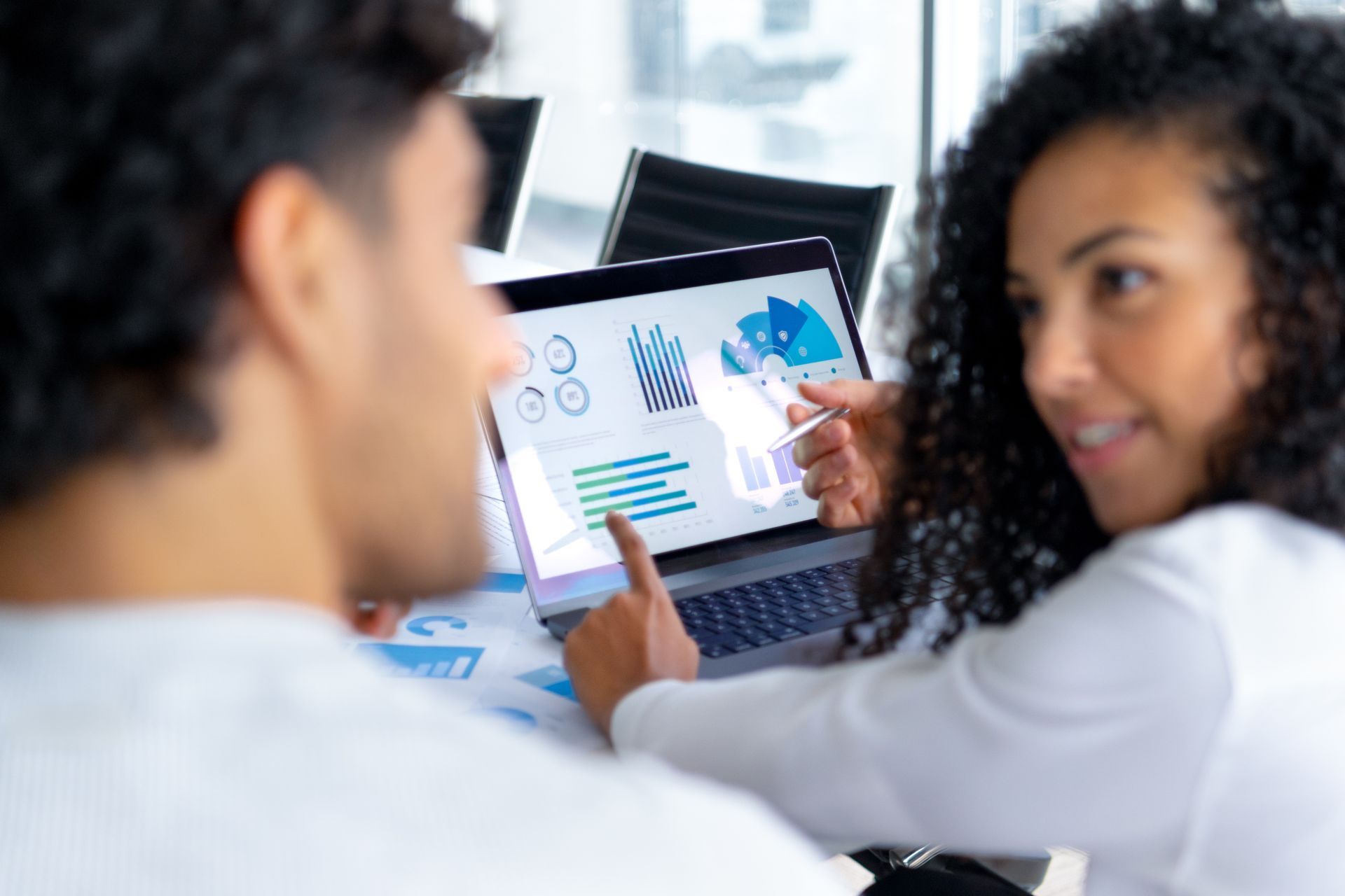 Two people looking at laptop screen with graphs and charts, office setting.
