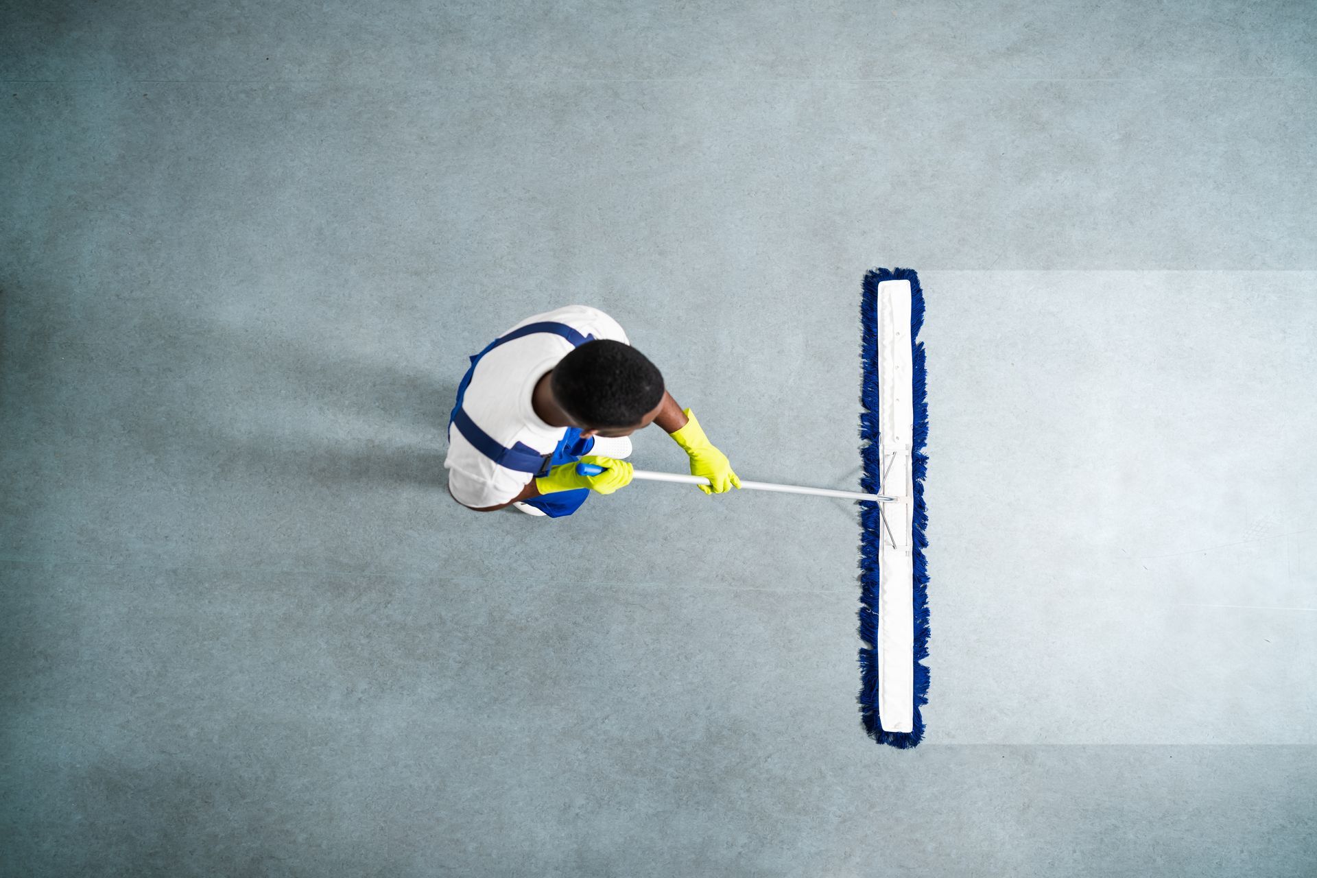 Person mopping a light-colored floor with a long blue and white mop, viewed from above.
