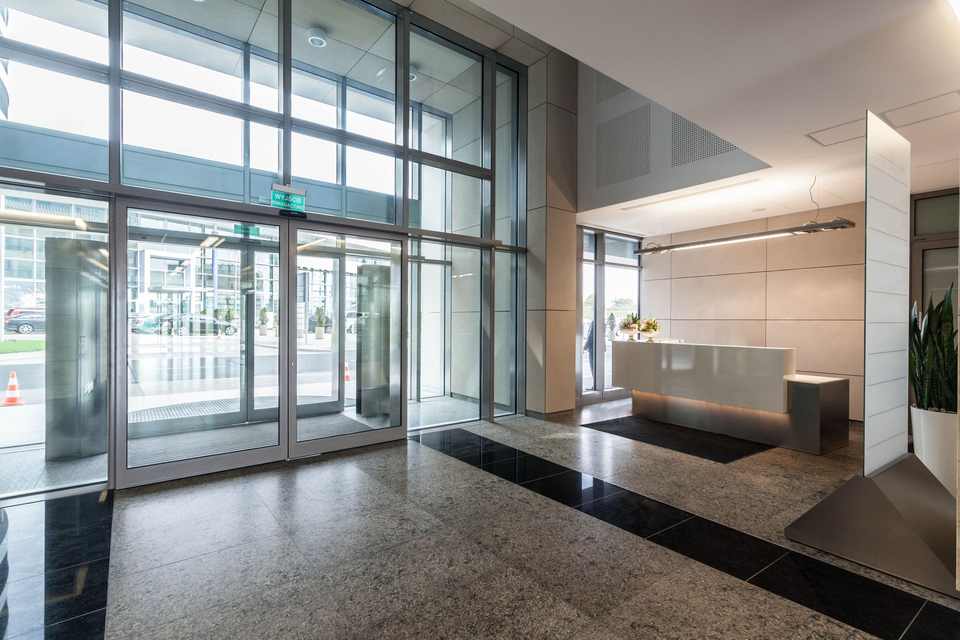 Modern office building entrance with revolving doors, reception desk, and gray terrazzo flooring.