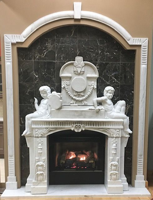 Ornate white fireplace surround with cherubs and a lit fire inset in a dark marble wall