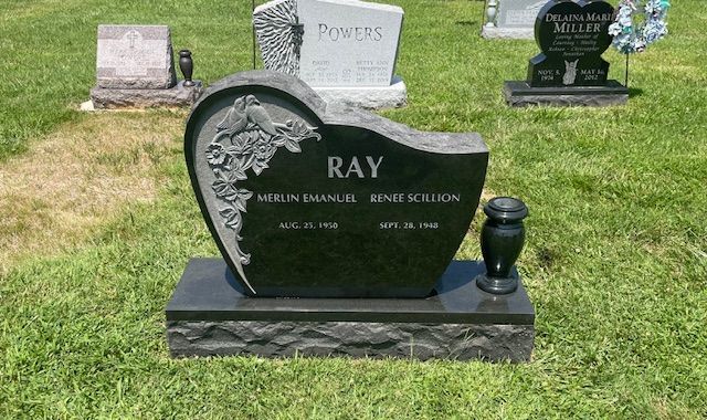 Heart-shaped black gravestone on a grassy cemetery lawn with floral engraving and the name Ray.