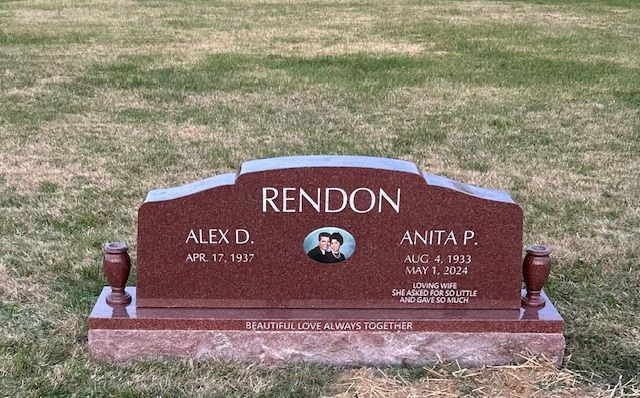 Maroon memorial headstone on grass with “RENDON” engraved and two small vase ornaments.