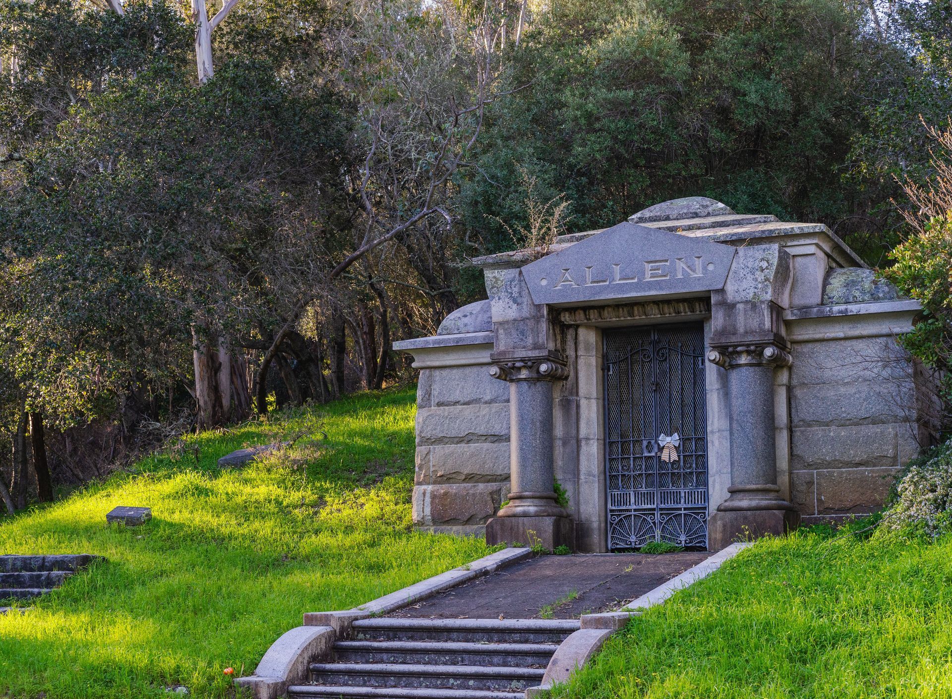 Stone mausoleum entrance on a grassy hillside with steps and trees behind it
