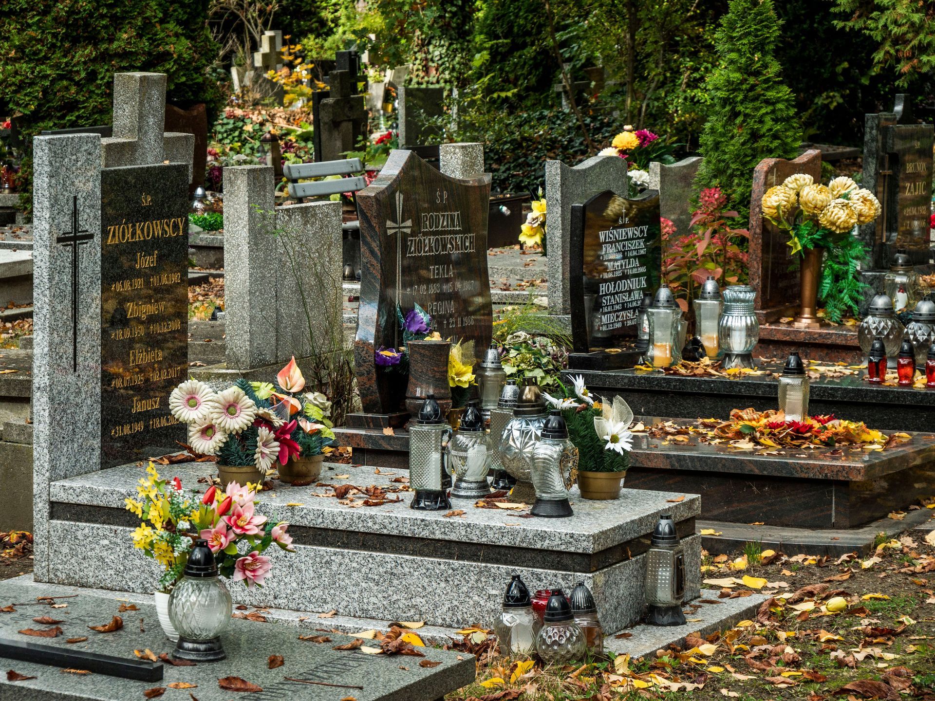 Flower-covered cemetery graves with candles and bouquets in a wooded area