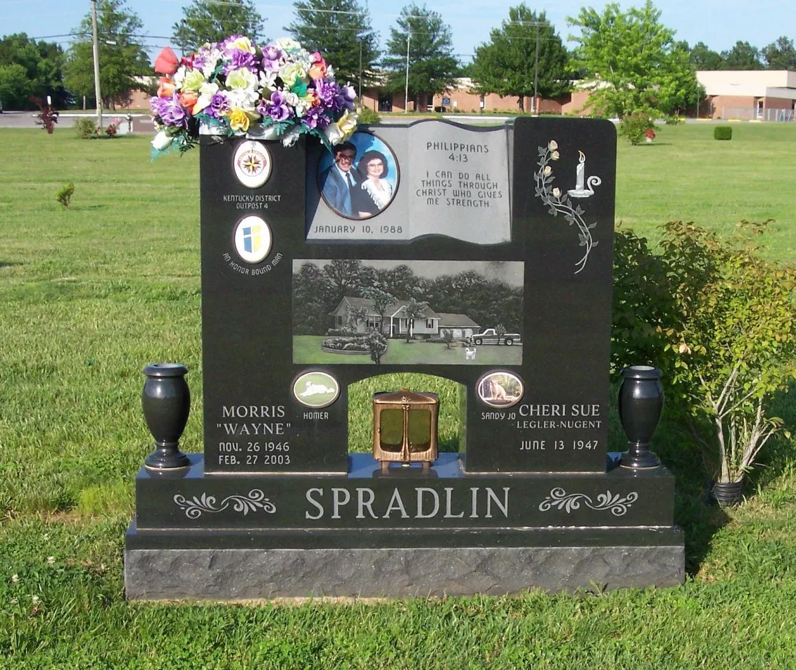 Black granite memorial headstone with flower arrangements in a grassy cemetery.