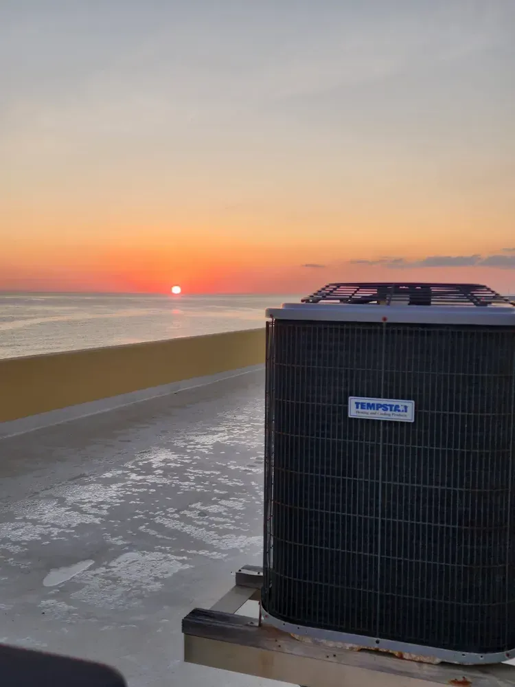 Air conditioner on a rooftop overlooking a sunset over the ocean. Orange sky, yellow wall.