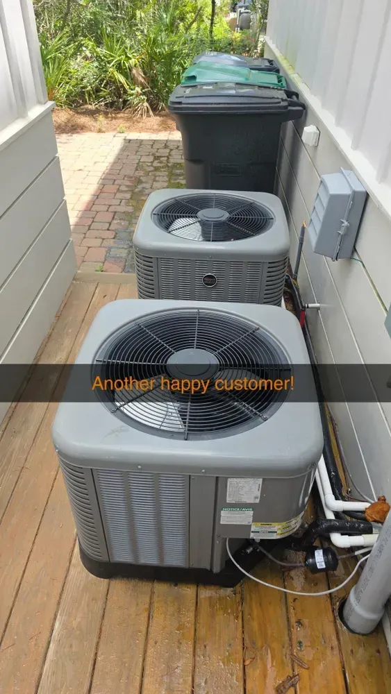 Two air conditioning units beside a wall, with trash cans in the background. 