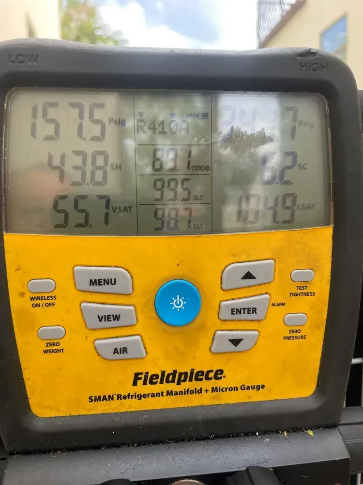 Close-up of a yellow and black Fieldpiece refrigerant manifold measuring pressures and temperatures in an outdoor setting.