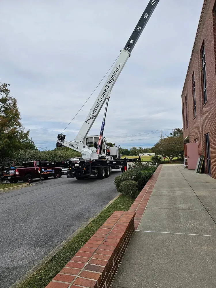Crane next to a brick building. The crane's arm is extended. A truck is parked on the street. Overcast sky.